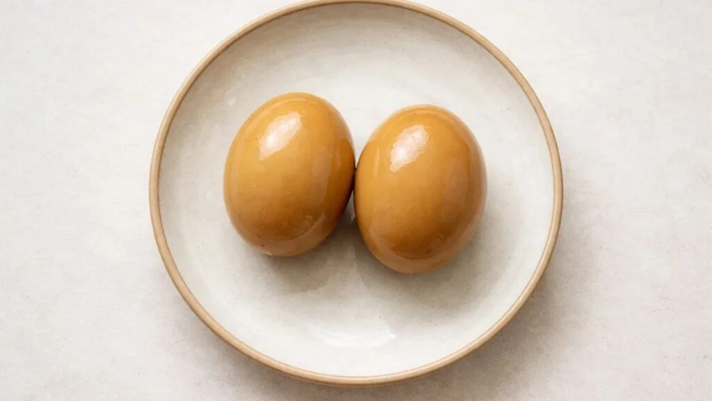 Whole soy sauce eggs with lightly stained whites on a ceramic plate