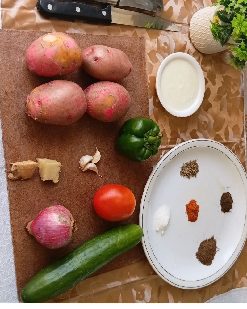 Raw ingredients for red potato salad recipe including red potatoes, Greek yogurt, cherry tomatoes, green pepper, red onion, garlic, and fresh dill arranged on a wooden surface
