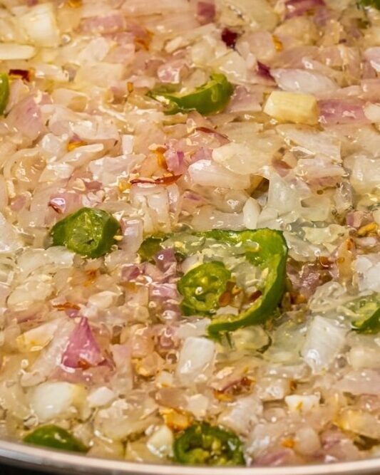 Place your skillet over medium heat and add the olive oil or ghee. Once hot, toss in your chopped onions, minced garlic, and sliced green chilies. Saute for roughly 2 to 3 minutes.