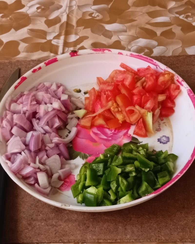 Freshly chopped red onion, green bell pepper, cherry tomatoes, and minced garlic on a wooden cutting board for red potato salad recipe