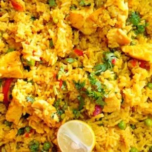 Overhead photo of healthy chicken yellow rice with turmeric, peas, and fresh cilantro in a ceramic bowl