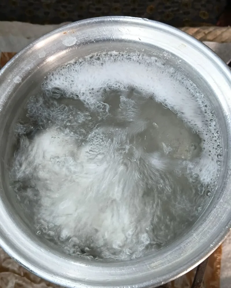 Hand lowering a whole egg into a pot of boiling water with a slotted spoon
