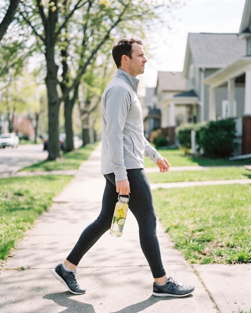 Woman walking outdoors while holding a water bottle infused with lemon and cucumber slices
